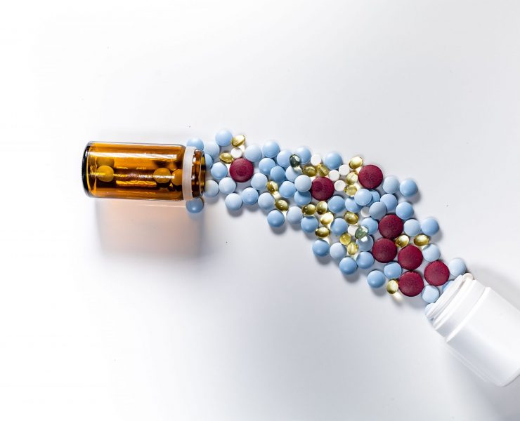 A top view of several colorful pills spilling from a glass and plastic bottles on a white background